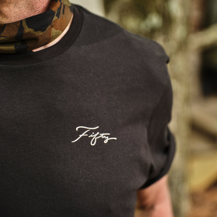 Person wearing a black t-shirt with 'Fifty' logo in a forest setting