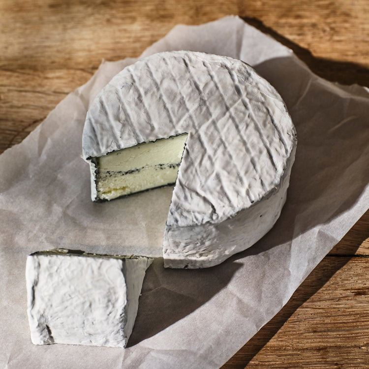 Round cheese with a slice removed on brown paper over a wooden surface