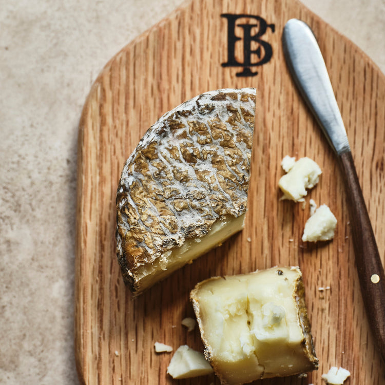 Wooden cutting board with a wedge of cheese and a knife on a textured surface