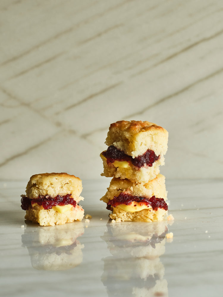 Three small jam-filled pastries stacked on a reflective surface with a neutral background