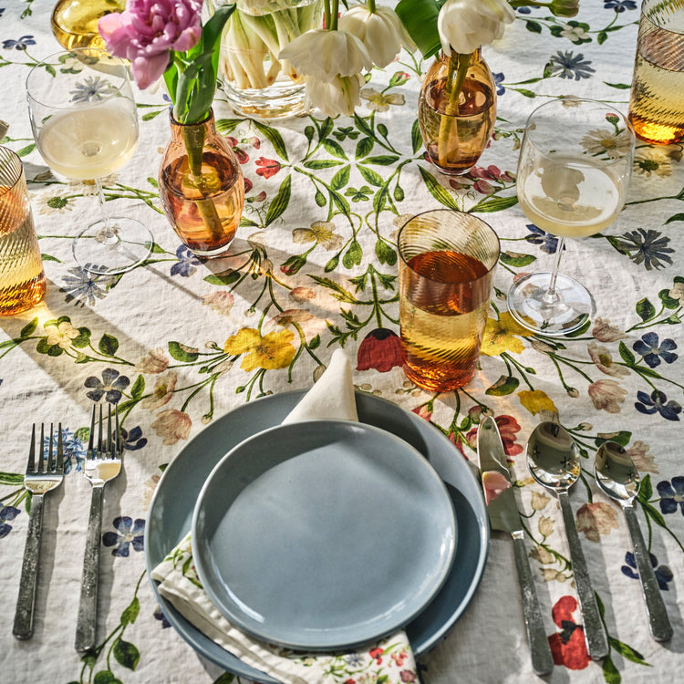 Dining table setting with floral tablecloth, plates, glasses, and cutlery.