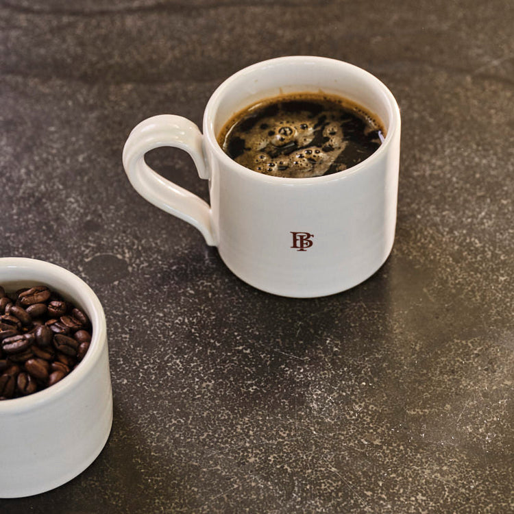 Two white mugs with coffee and coffee beans on a dark stone surface