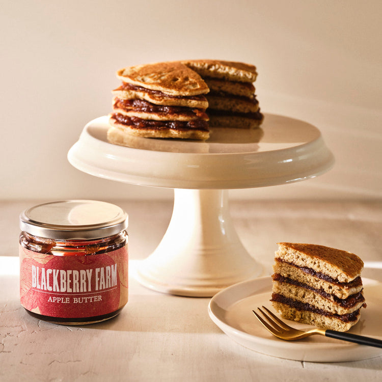 Stack of pancakes with a slice on a plate and a jar of Blackberry Farm apple butter.