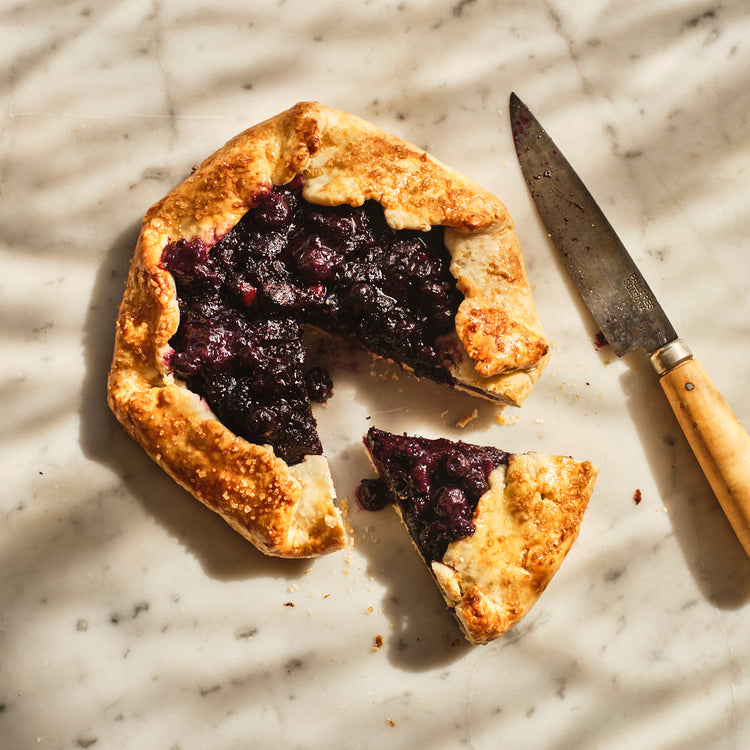 Blueberry galette with a slice removed on a marble surface with a knife.