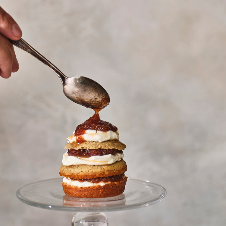 Stack of layered cupcakes being topped with a spoonful of jam on a neutral background