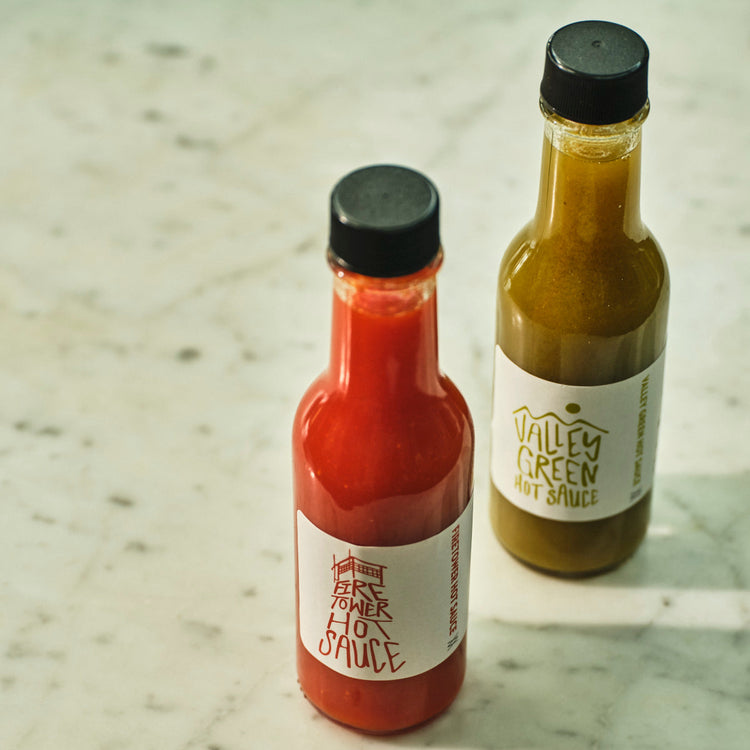 Two bottles of hot sauce on a marble surface