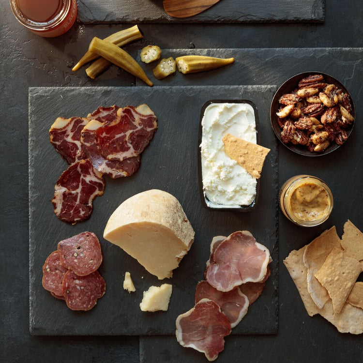 Plated charcuterie board with meats, cheeses, and accompaniments on a dark surface.