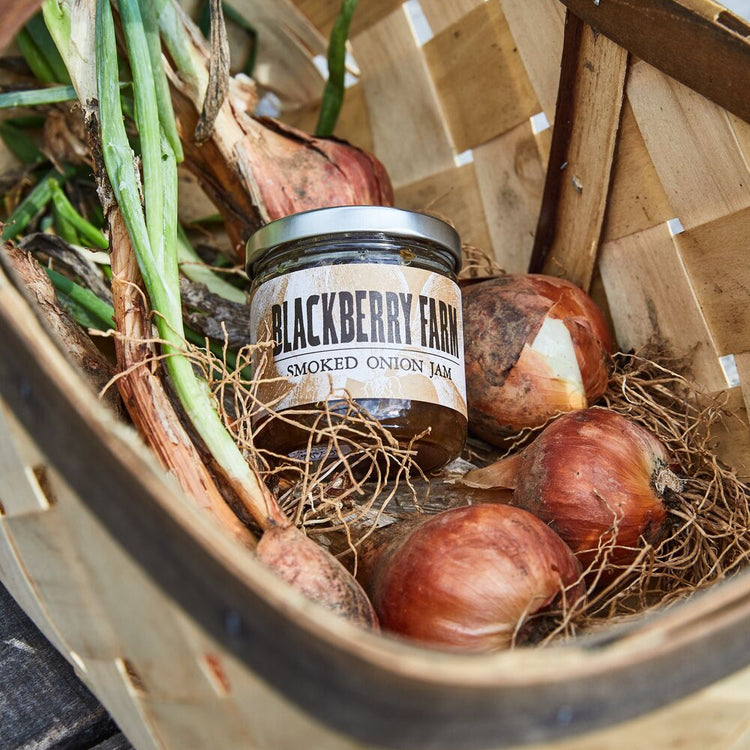 Jar of Blackberry Farm smoked onion jam in a basket with onions and green onions.