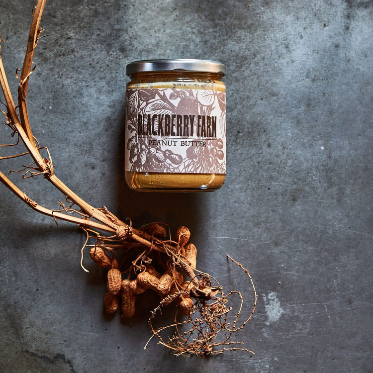Jar of peanut butter with a rustic label on a textured surface with peanuts and roots.