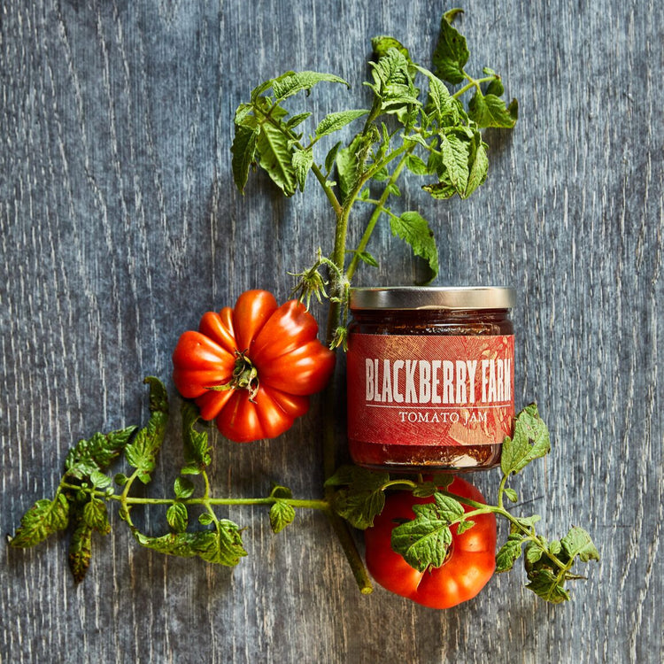 Jar of Blackberry Farm tomato jam with fresh tomatoes and leaves on a wooden surface