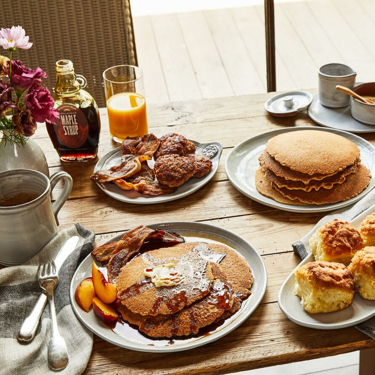 Breakfast table with pancakes, bacon, scones, and various condiments.