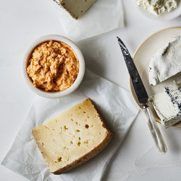 Assorted cheeses on a white surface with a knife and small dishes of spreads.