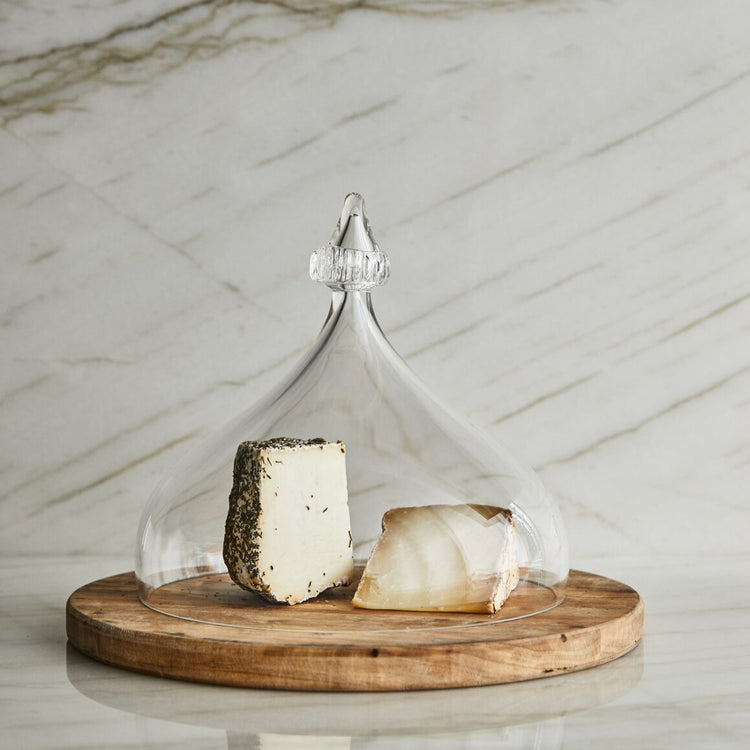 Two types of cheese under a glass dome on a wooden board with a marble background
