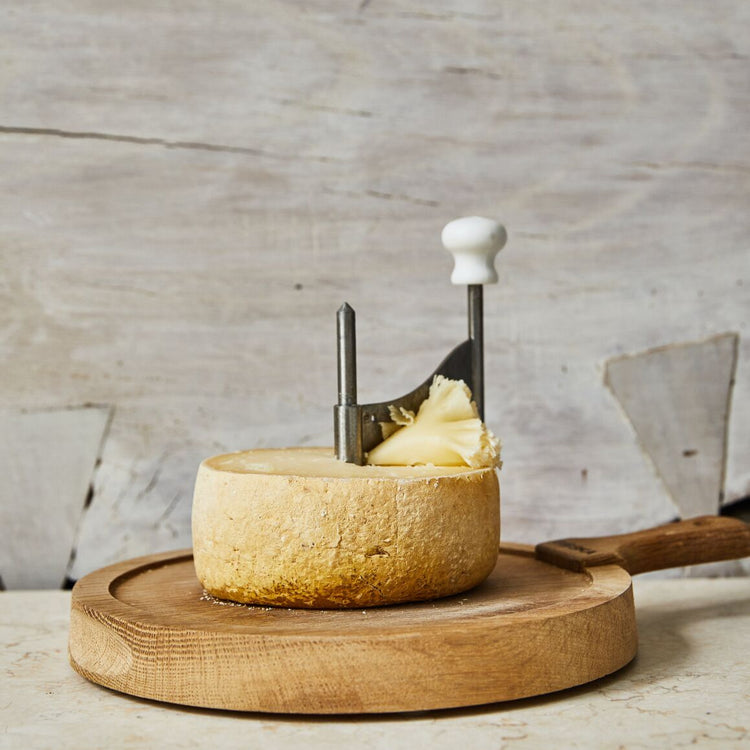 Round wheel of cheese with a cheese slicer on a wooden board against a rustic background