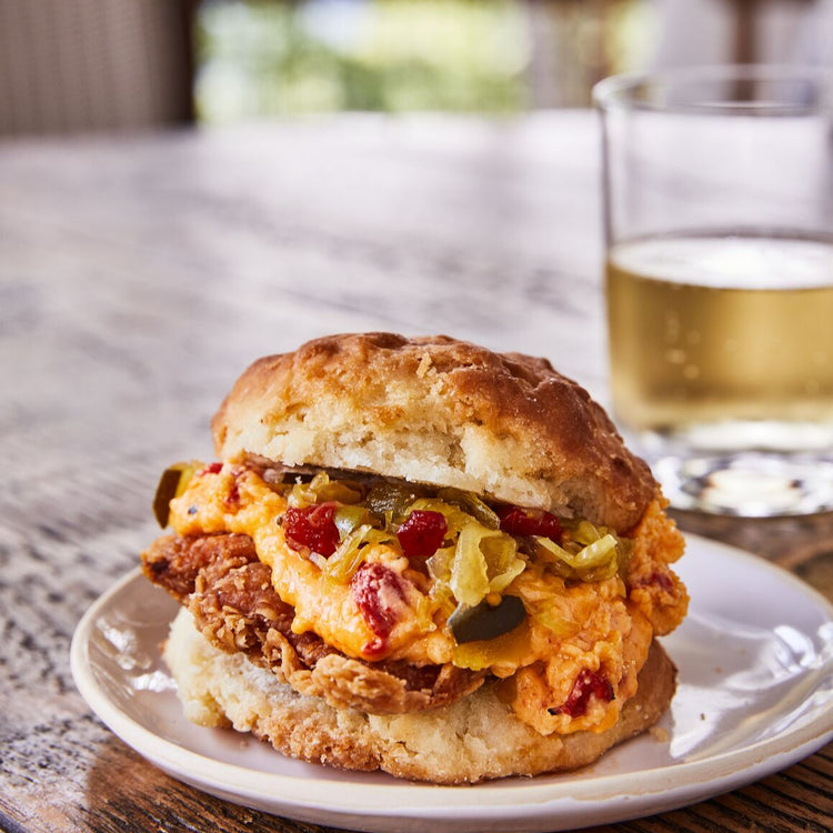 Biscuit sandwich with pimento cheese on a plate with a glass of beer in the background.
