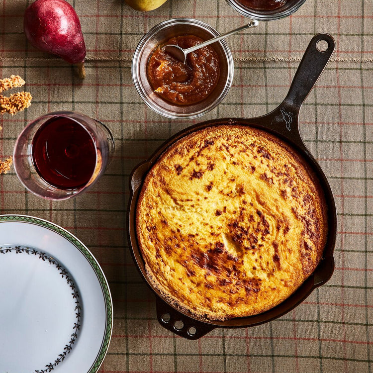 Skillet of cornbread with jars of jam on a checkered tablecloth