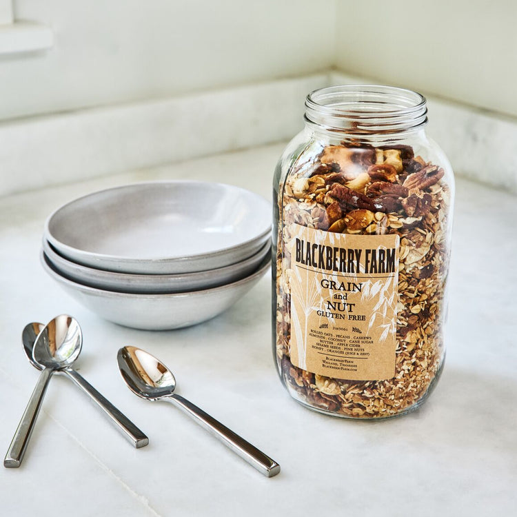 Jar of Blackberry Farm granola on a kitchen counter with bowls and spoons.