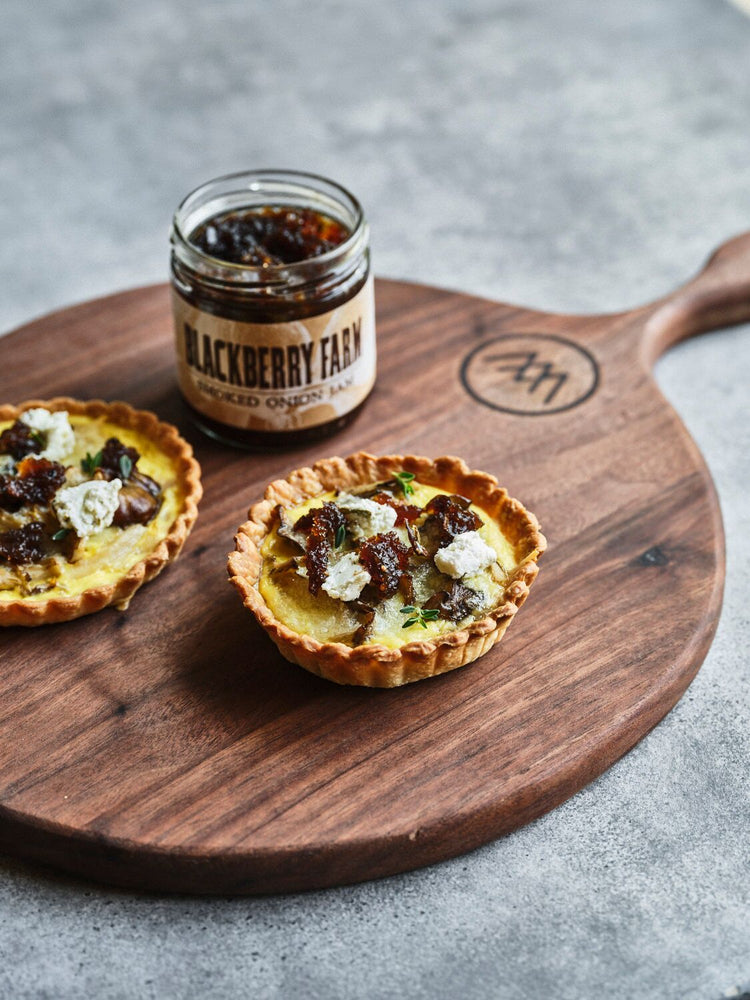 Two small pies with a jar of jam on a wooden board with 'Blackberry Farm' branding.