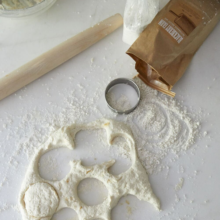 Dough with cut-out shapes on a floured surface with a rolling pin and cookie cutter.
