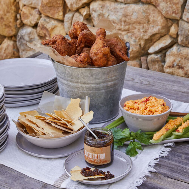 Outdoor setting with fried chicken, chips, and dips on a rustic stone wall background